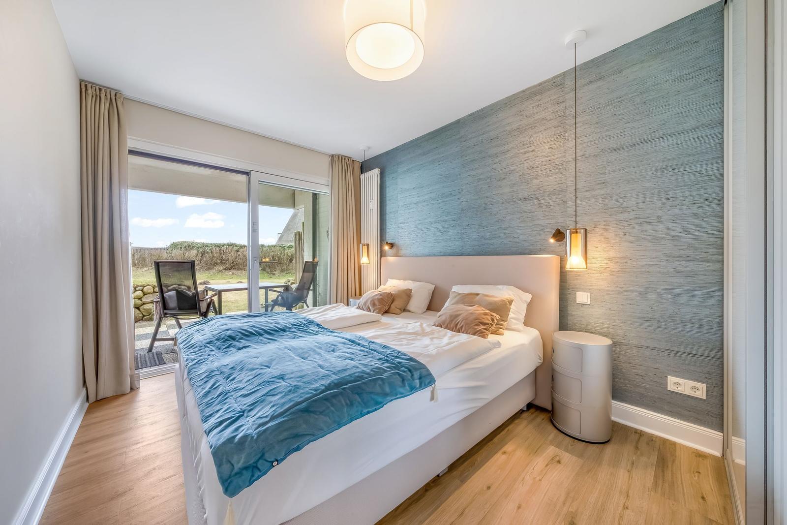 Schlafzimmer mit Bett, blauer Decke und Balkonansicht.