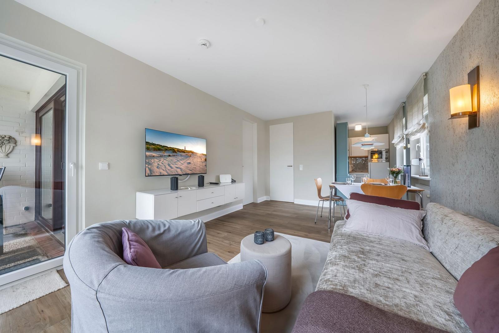 Wohn- und Essbereich mit TV, Sofa und Küchenbereich im Hintergrund.