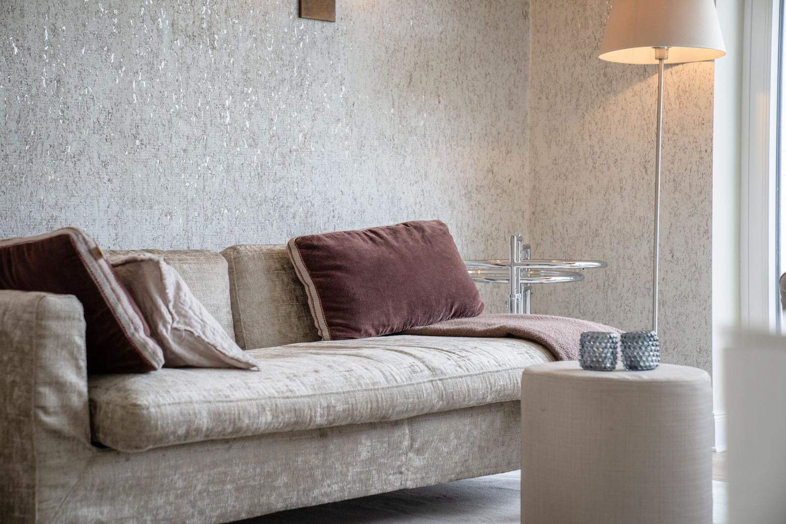 Ein Sofa mit Kissen, Beistelltisch und Stehlampe vor einer texturierten Wand.