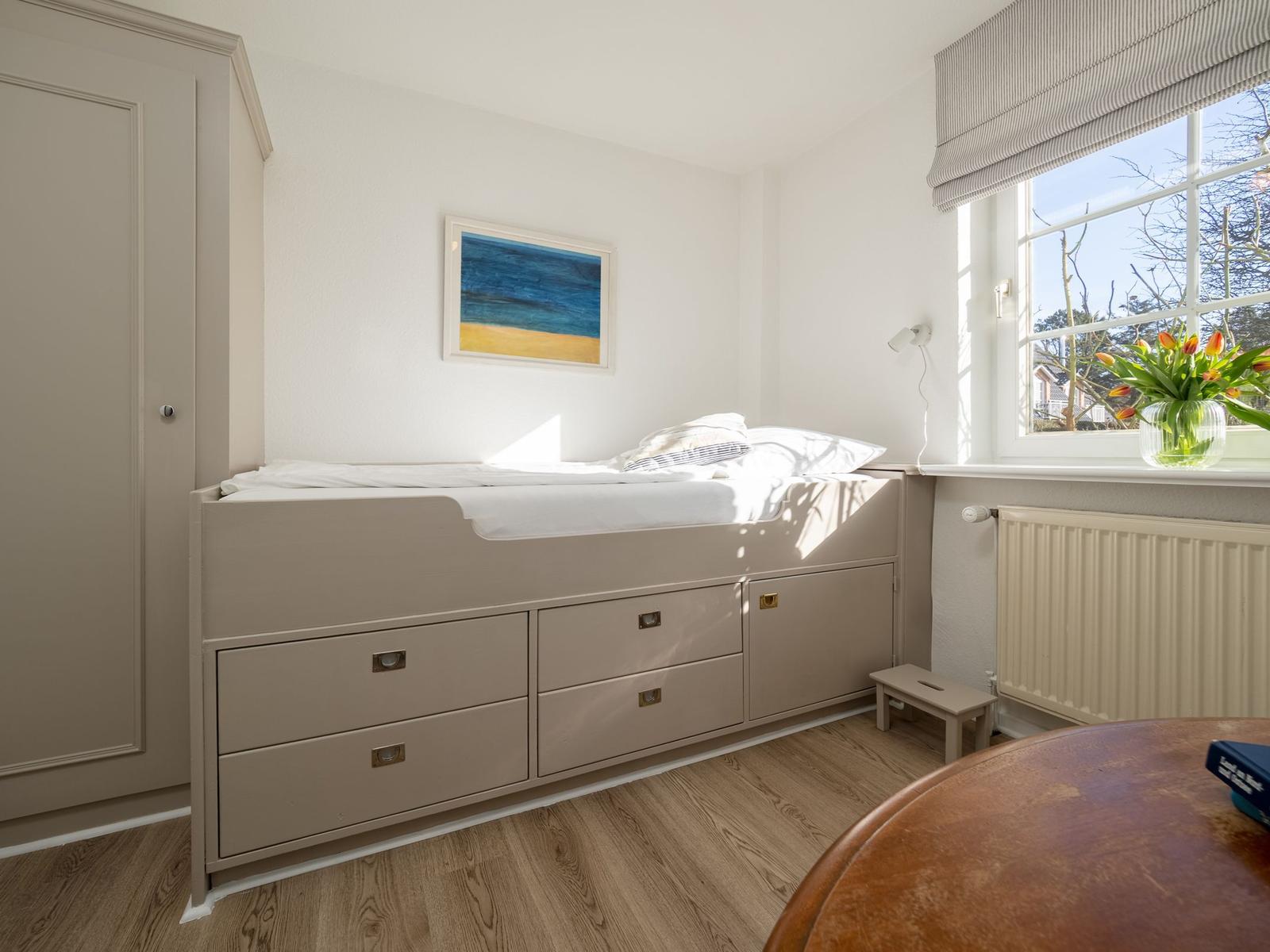 Schlafzimmer mit Bett, Schrank und Fenster mit Blumen.