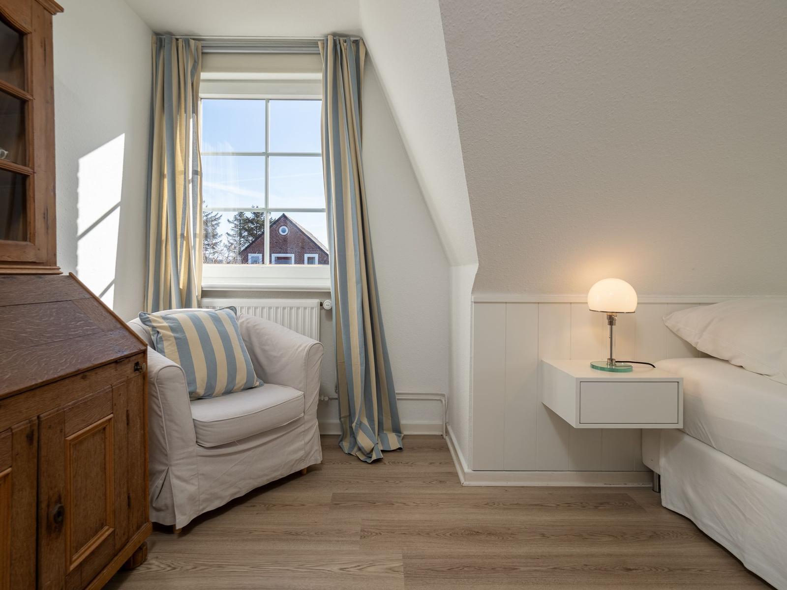Schlafzimmer mit Bett, Nachttisch, Lampe und Fenster mit Blick auf Haus