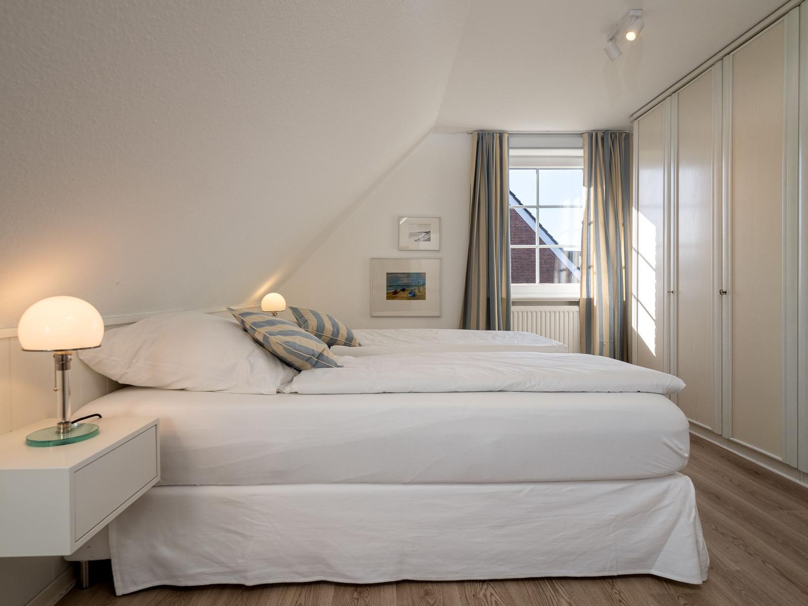 Schlafzimmer mit Doppelbett, Nachttisch, Gardinen und Kleiderschrank.