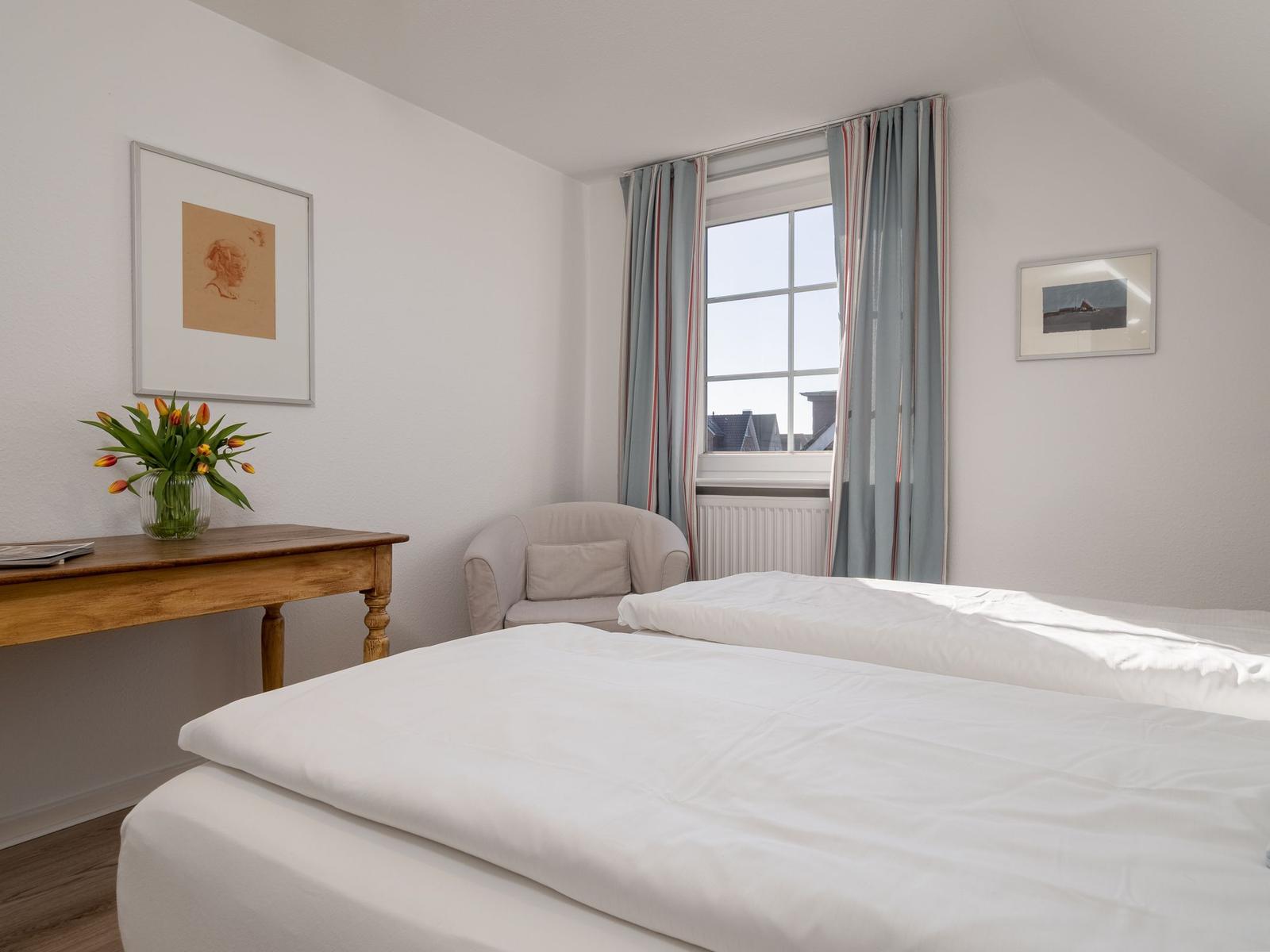 Ein Schlafzimmer mit einem Bett, einem Sessel und einem Tisch mit Blumen.