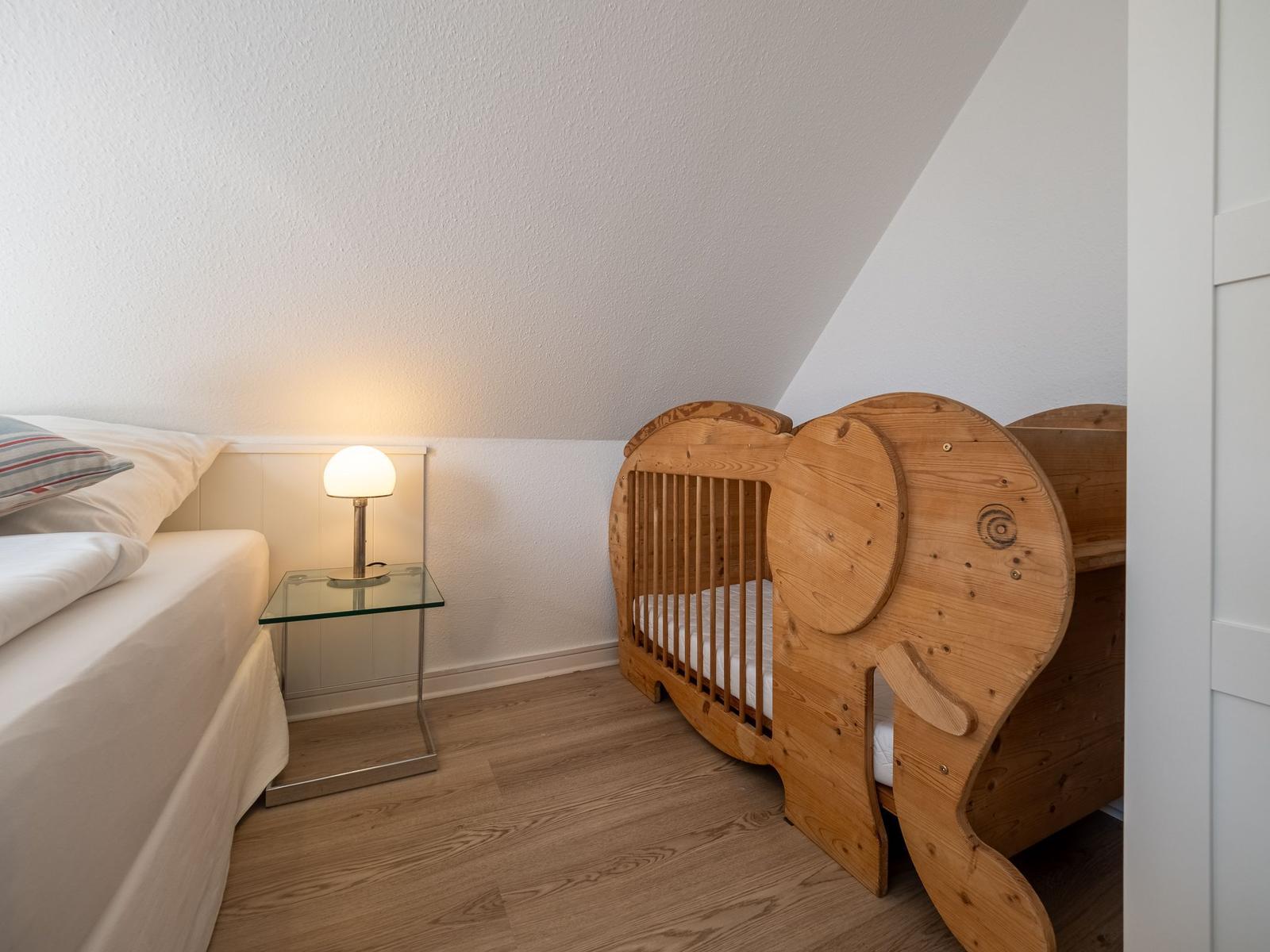 Schlafzimmer mit Babybett und Nachttisch unter schrägem Dach