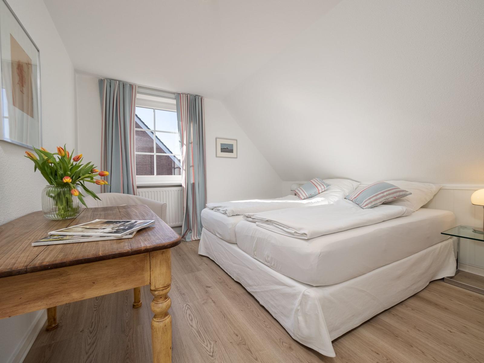 Schlafzimmer mit Dachschrägen, Bett, Tisch und Blumen.