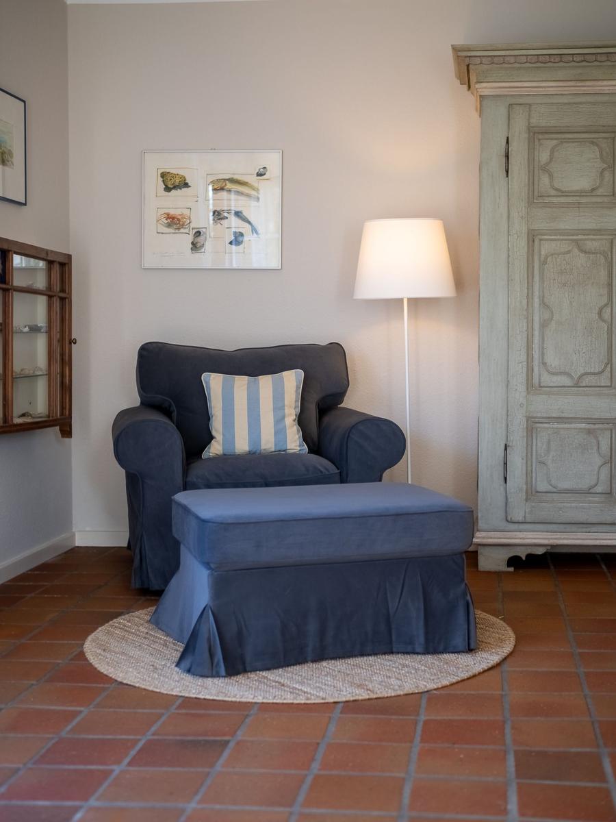 Ein Sessel mit Kissen und Beistelltisch auf Teppich vor Wand mit Bild und Lampen.