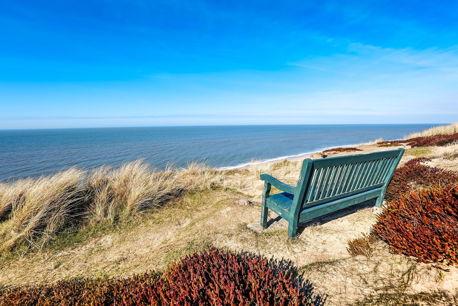A green wooden bench on a dune with a view of the sea and sky.
