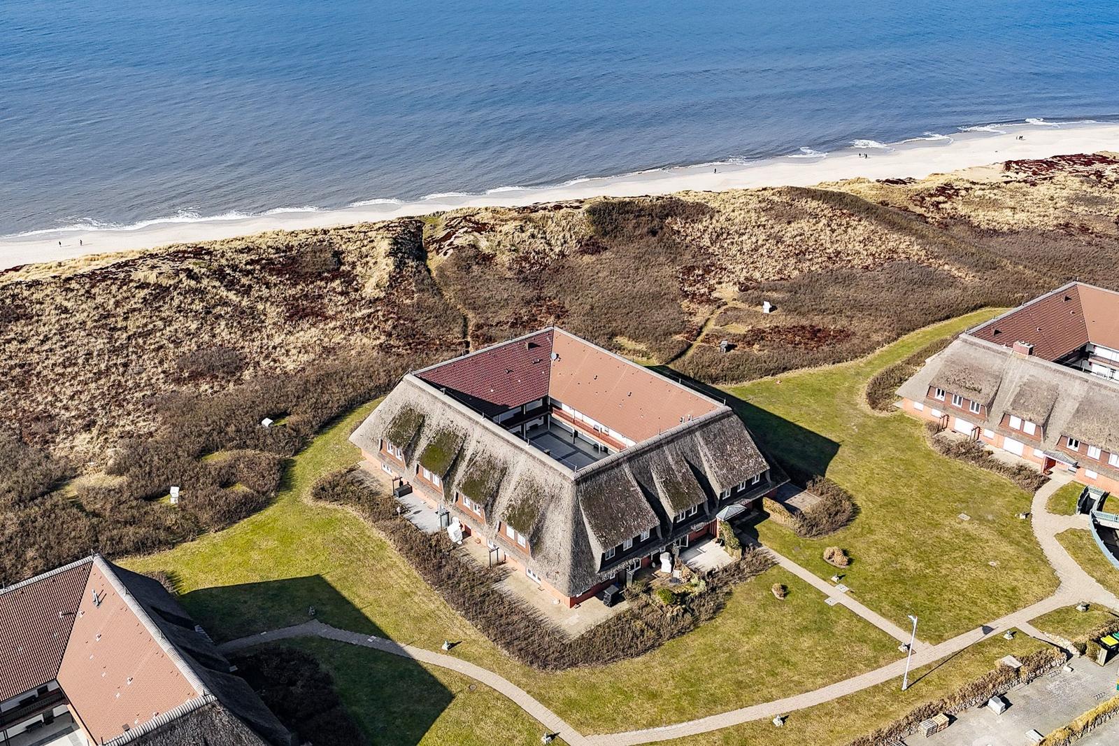 House with thatched roof is directly on the beach. Green lawns and walking paths surround the property.
