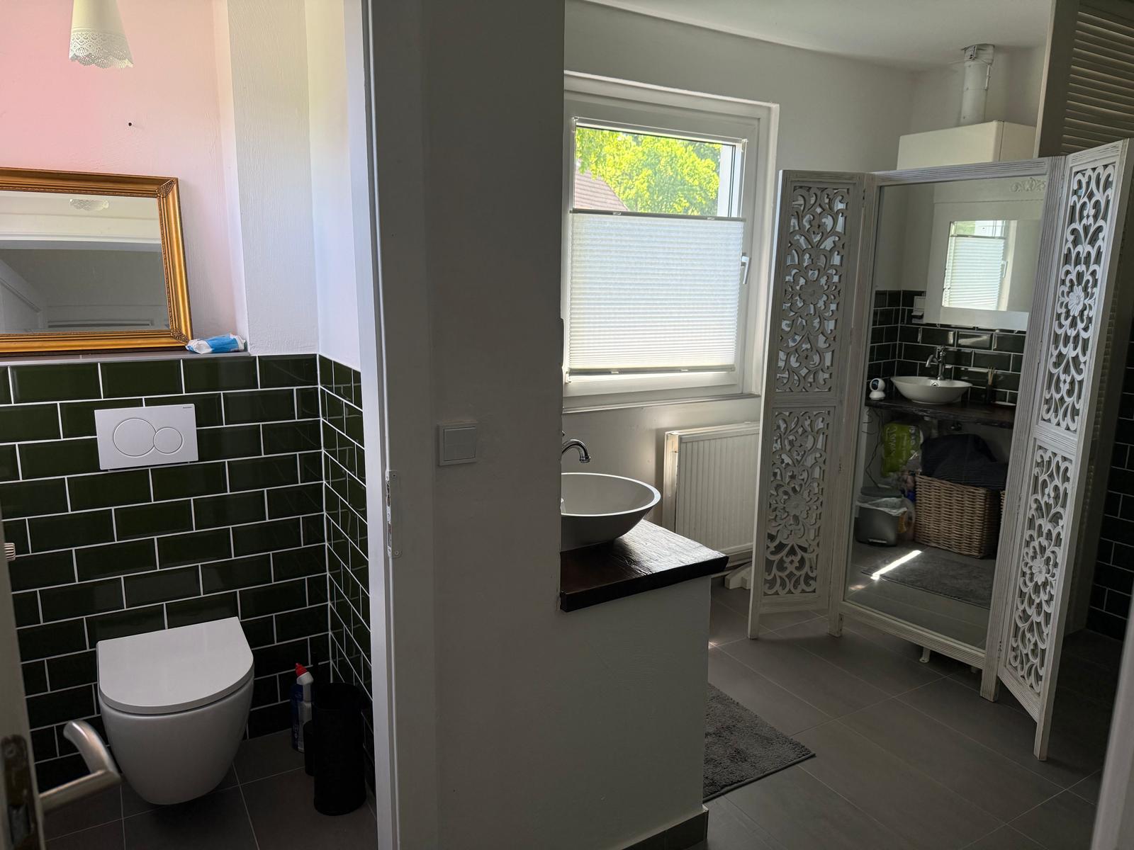 Badezimmer mit Toilette, Waschbecken und Duschbereich mit Fenster.