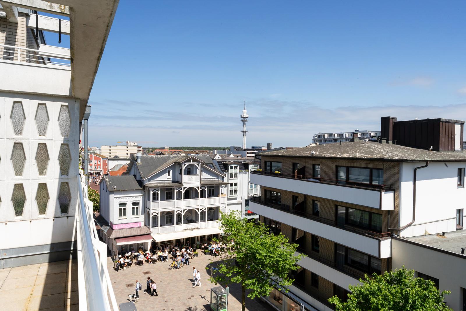 Blick auf eine belebte Straße mit Gebäuden und einem Turm im Hintergrund.
