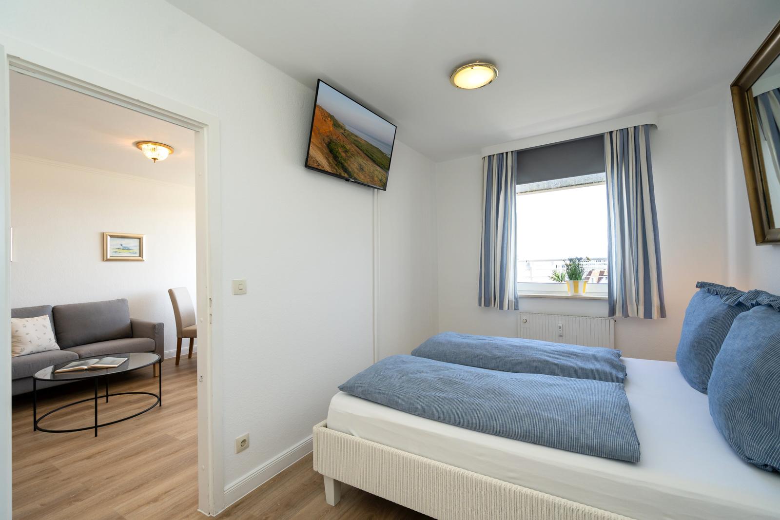 Schlafzimmer mit Bett, TV und Blick auf Balkon. Durchgang in Wohnbereich mit Sofa.