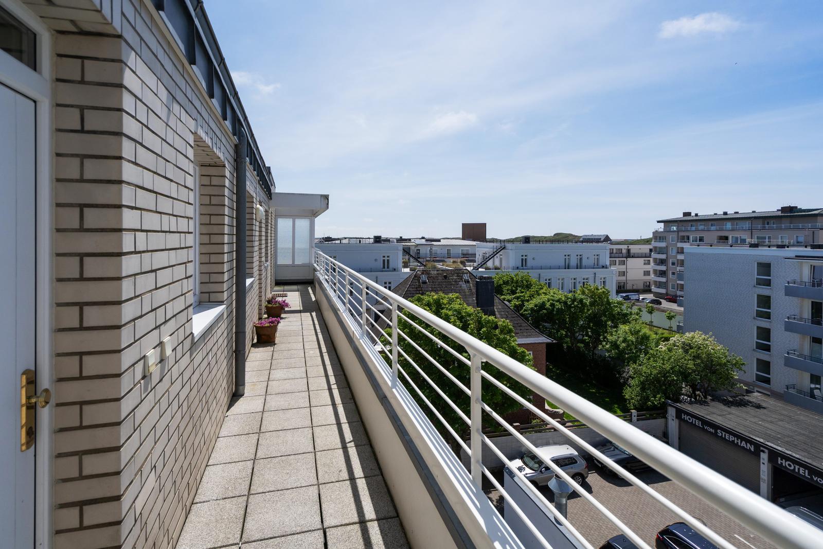 Terrasse mit weißer Brüstung und Blick auf Gebäude und Bäume.