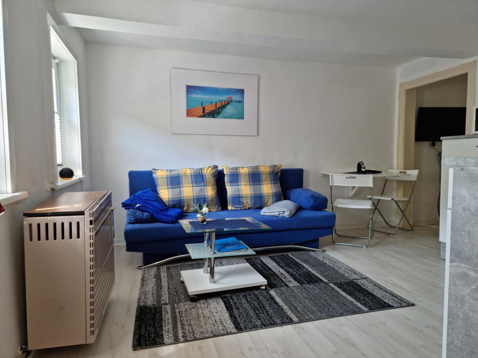 Blauer Sofa mit Kissen, Glas-Tisch und Teppich im Wohnzimmer.
