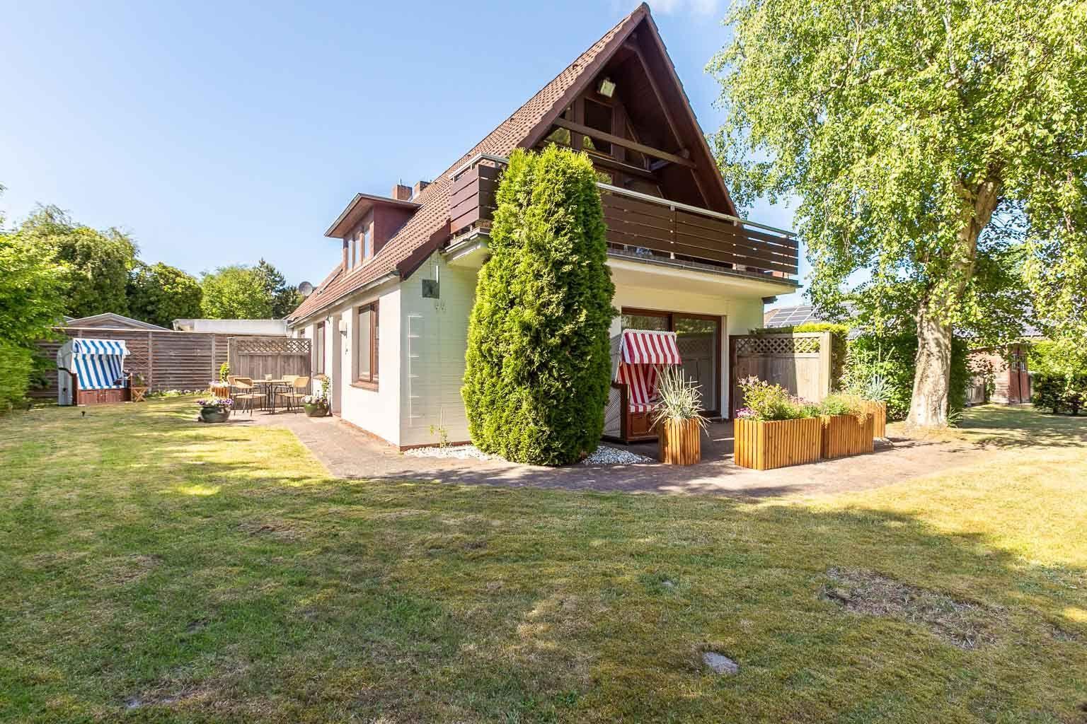Haus mit Balkon, Garten und Terrasse mit Gartenmöbeln und Pflanzen.