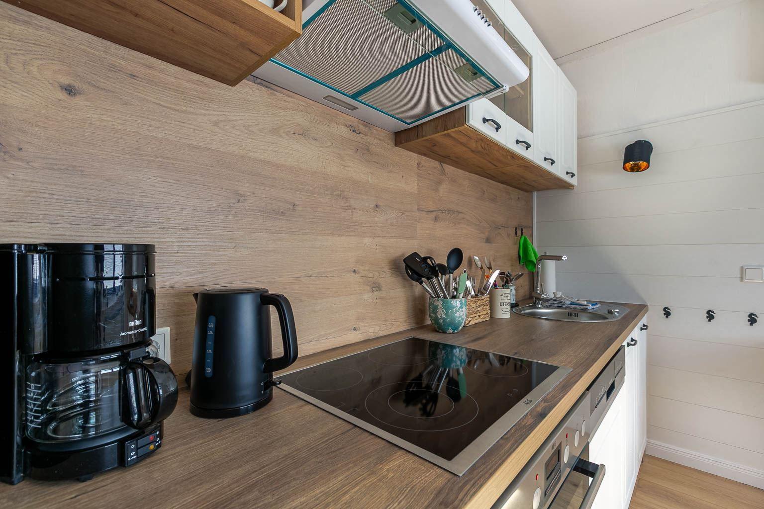 Küche mit Kochfeld, Kaffeemaschine und Wasserkocher auf Holzoberfläche.