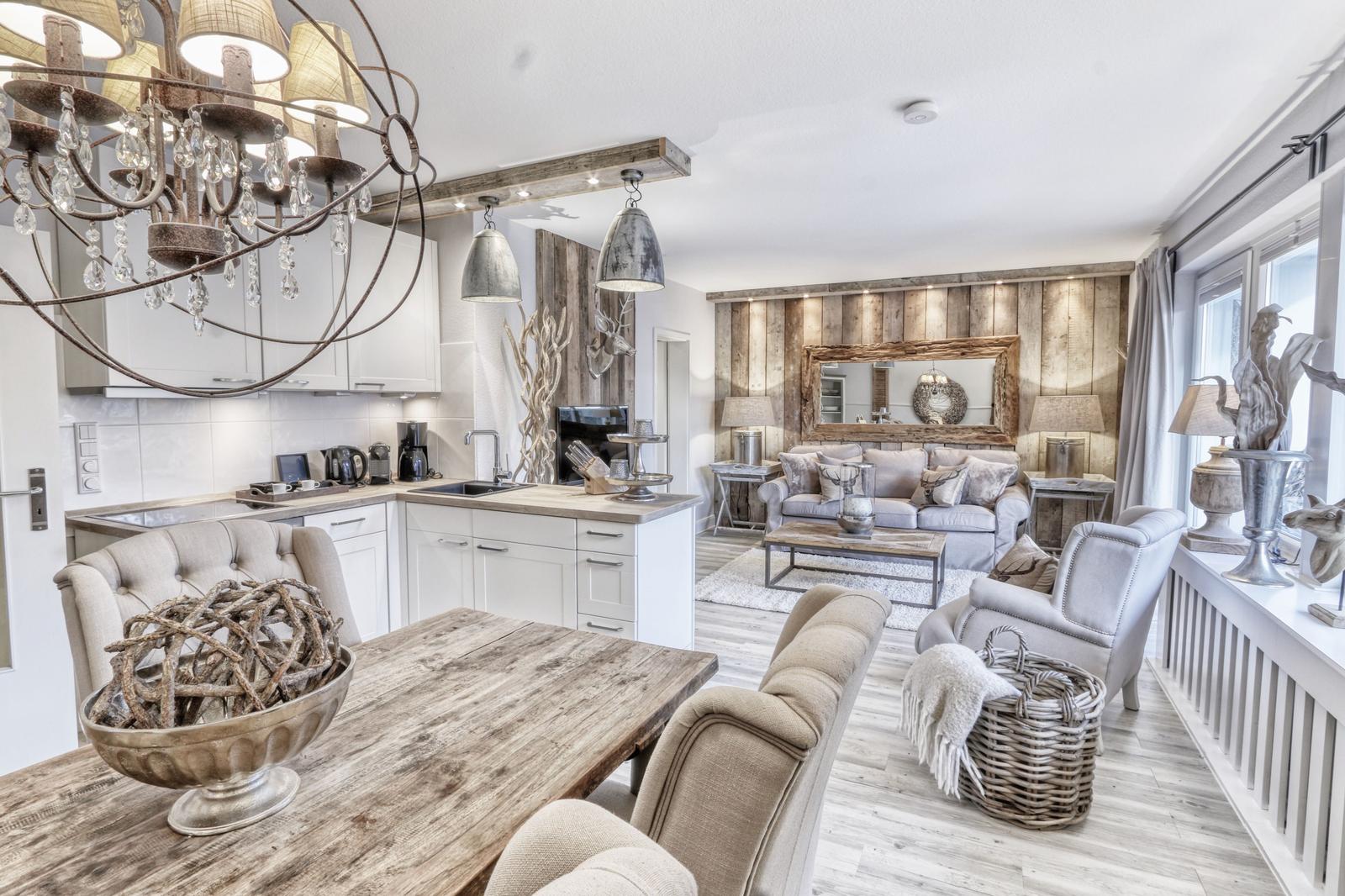 Essbereich mit Holztisch, Küche mit weißen Schränken und Wohnzimmer mit Sofa und Spiegel.