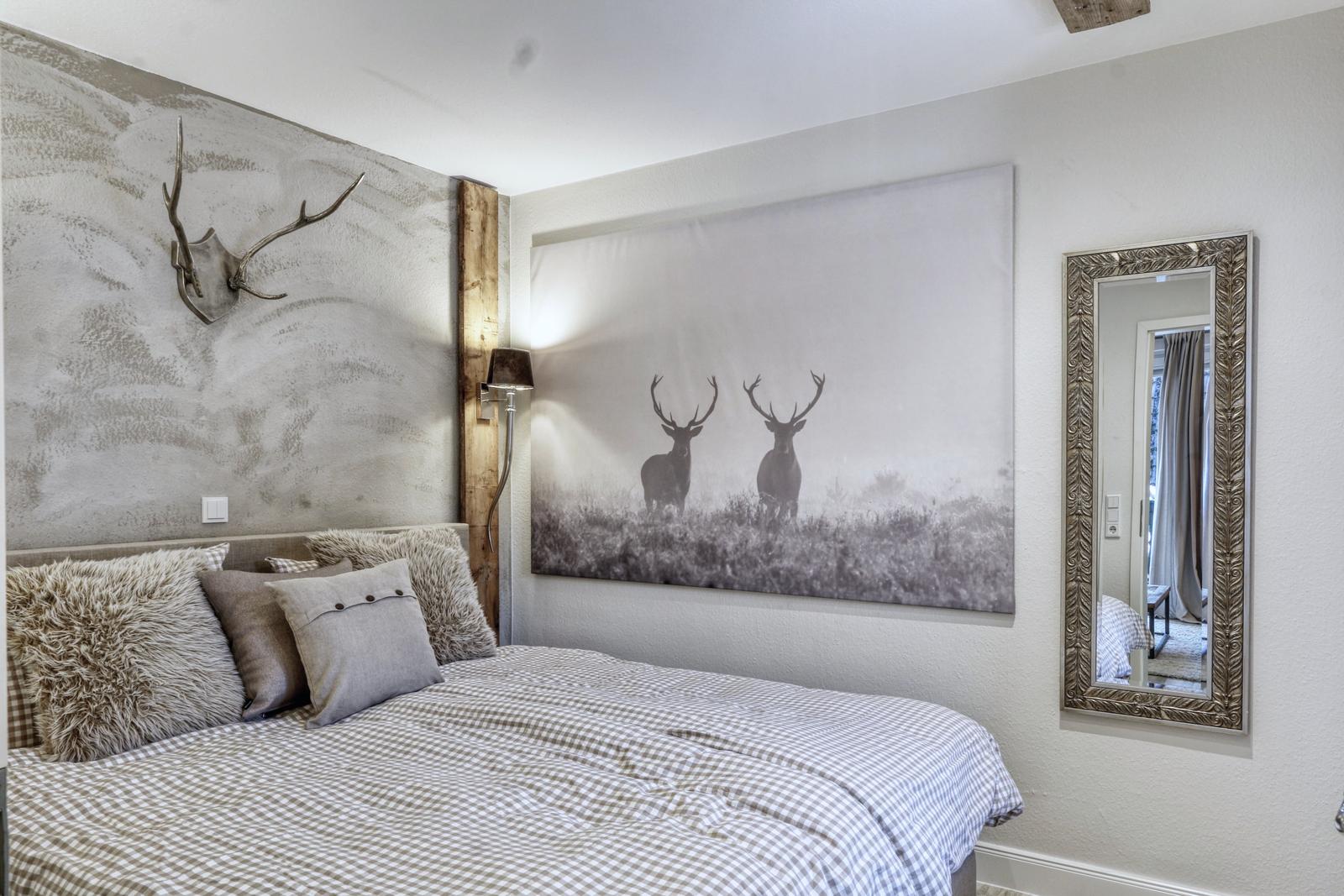 Schlafzimmer mit Bett, Wandbild von Hirschen und Spiegel.