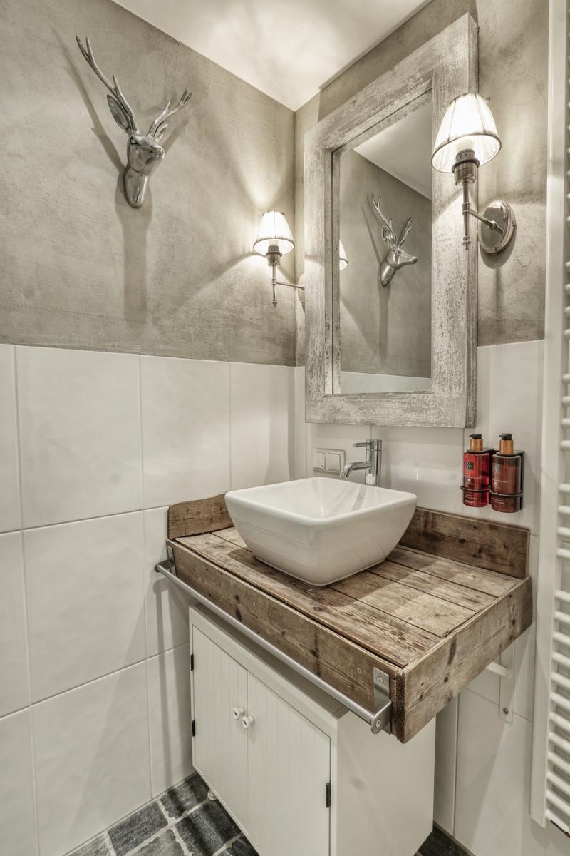 Badezimmer mit Waschbecken auf Holzplatte, Spiegel und Wandbeleuchtung.