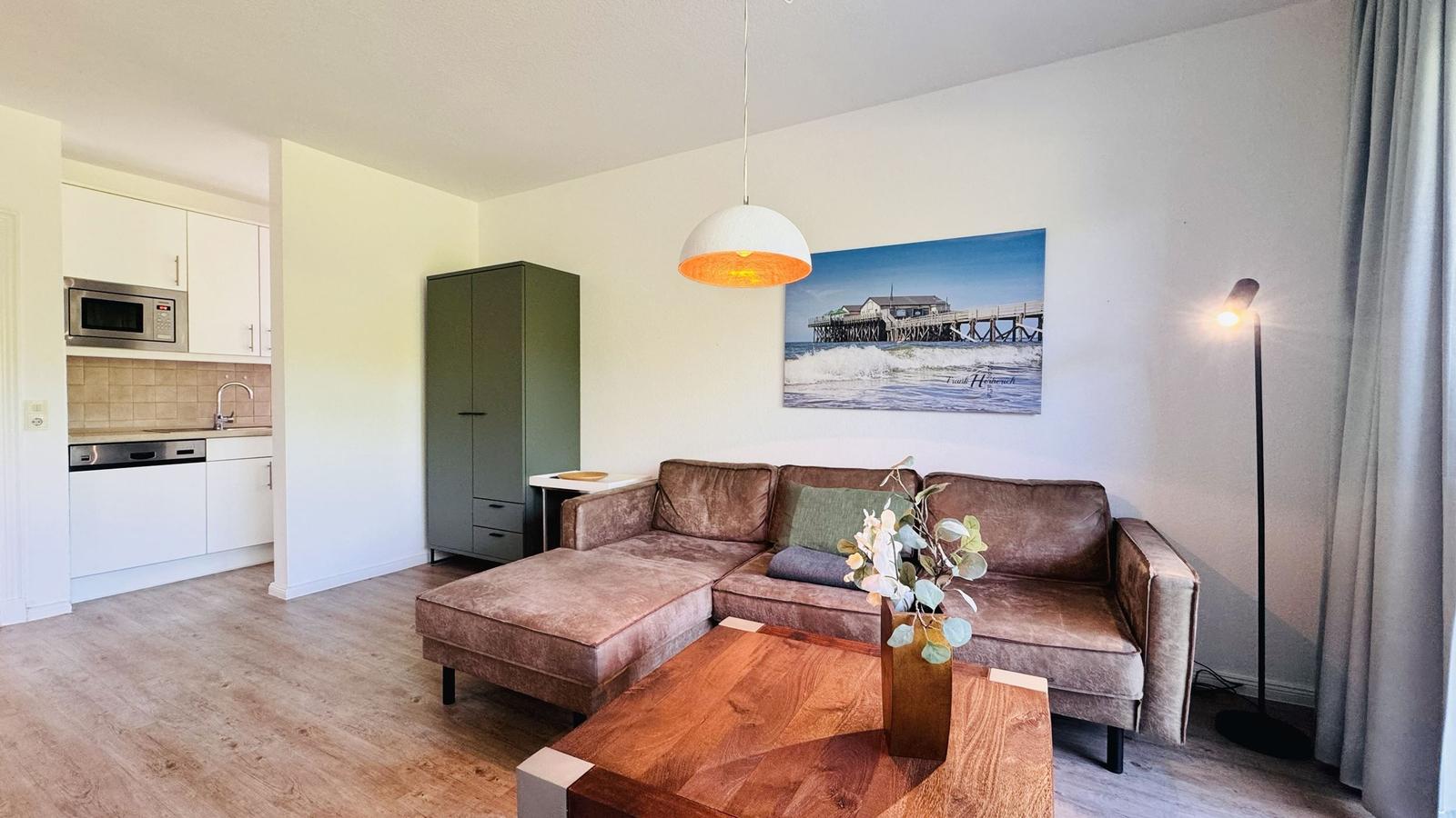 Wohnzimmer mit Sofa, Tisch und Küchenbereich im Hintergrund.