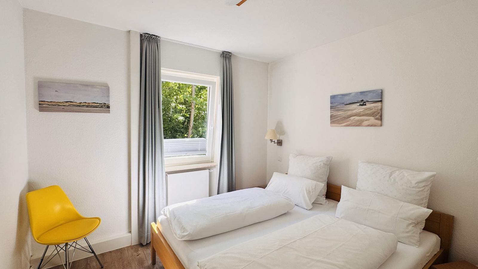 Ein Schlafzimmer mit einem Bett, einem Fenster und einer gelben Sitzgelegenheit.