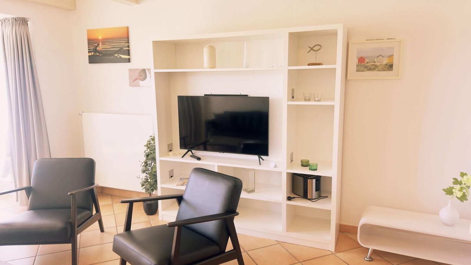 Wohnzimmer mit Fernseher, zwei Sesseln und weißen Regalen.