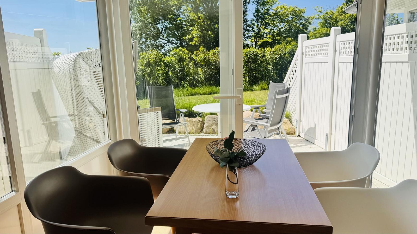Essbereich mit Tisch und Stühlen, Blick auf Terrasse mit Garten.