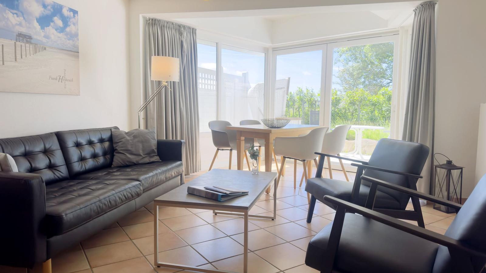 Wohn- und Essbereich mit Sofa, Stühlen und großem Fenster. Außenbereich mit Tisch und Stühlen.