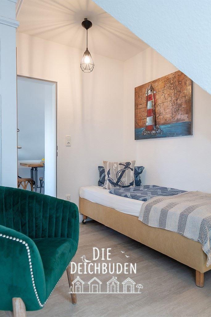 Schlafzimmer mit Bett, grünem Sofa und Leuchte. Wandbild zeigt Leuchtturm.