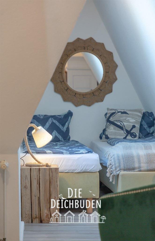Zwei Betten unter Dachschräge mit Seemotiv-Kissen und runden Spiegel.