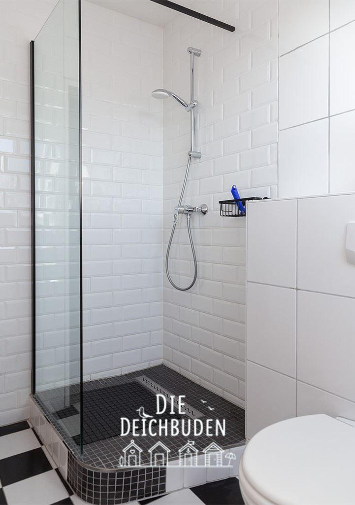 Dusche mit Glaswand, weißen Fliesen und schwarzer Bodenfliese.