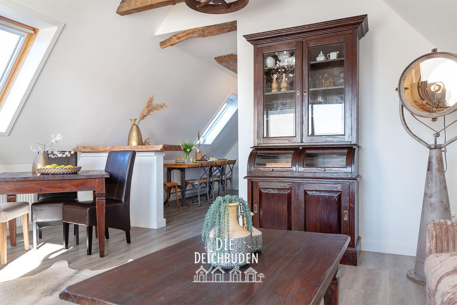 Essbereich mit Holztisch, dunklen Stühlen und einem hohen Schrank. Dachfenster und Holzbalken sichtbar.