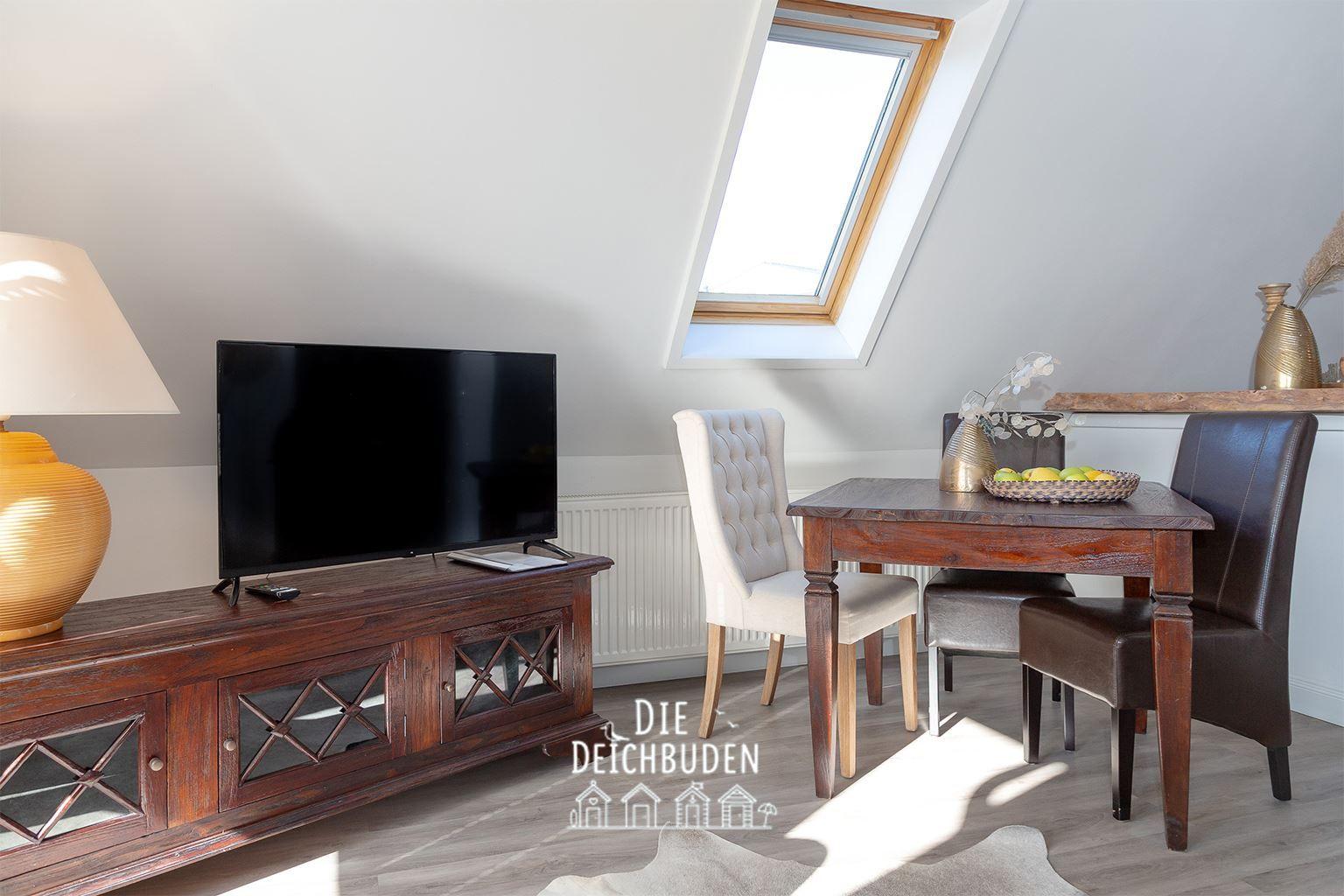 Ein Raum mit TV, Esstisch und Dachfenster. Holzmöbel und helles Ambiente.