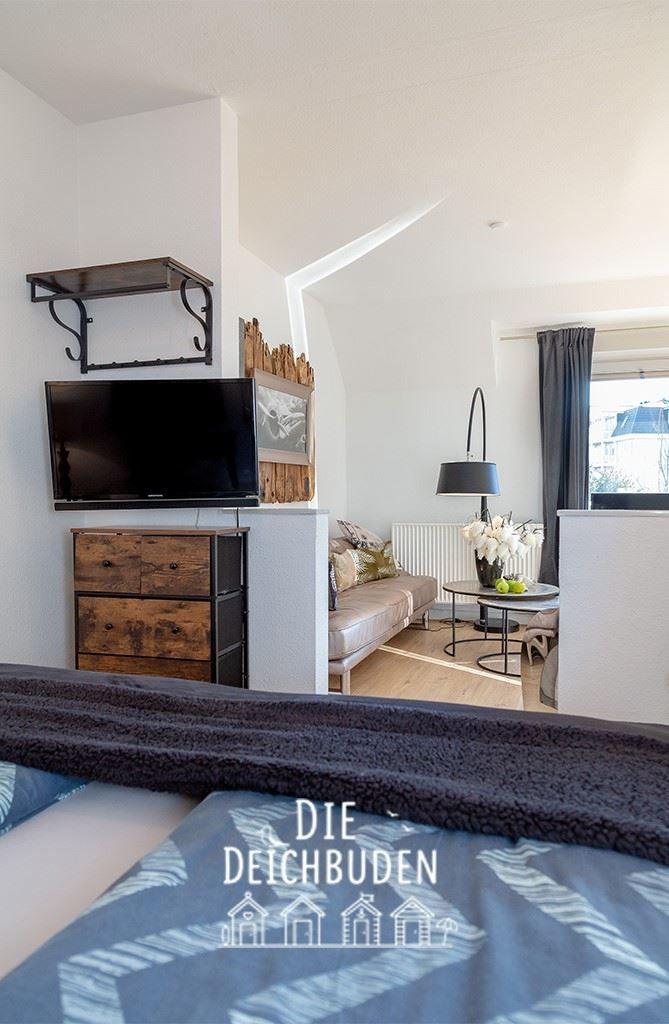 Schlafzimmer mit Blick auf Wohnbereich mit Sofa und TV.