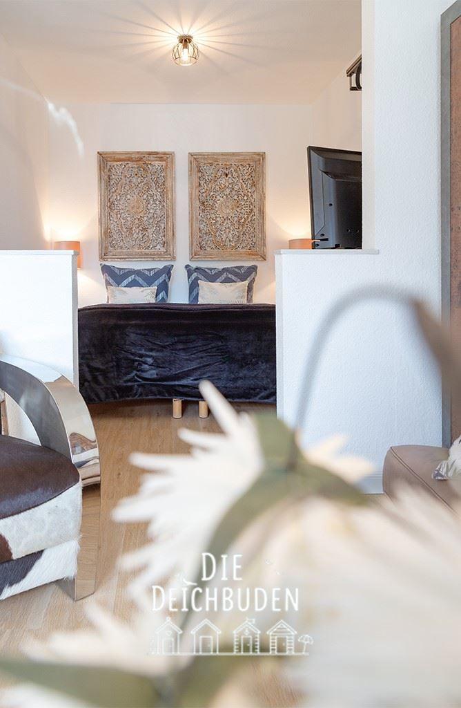 Schlafzimmer mit Bett, Wandbildern und Fernseher. Holzboden und dekorative Kissen.