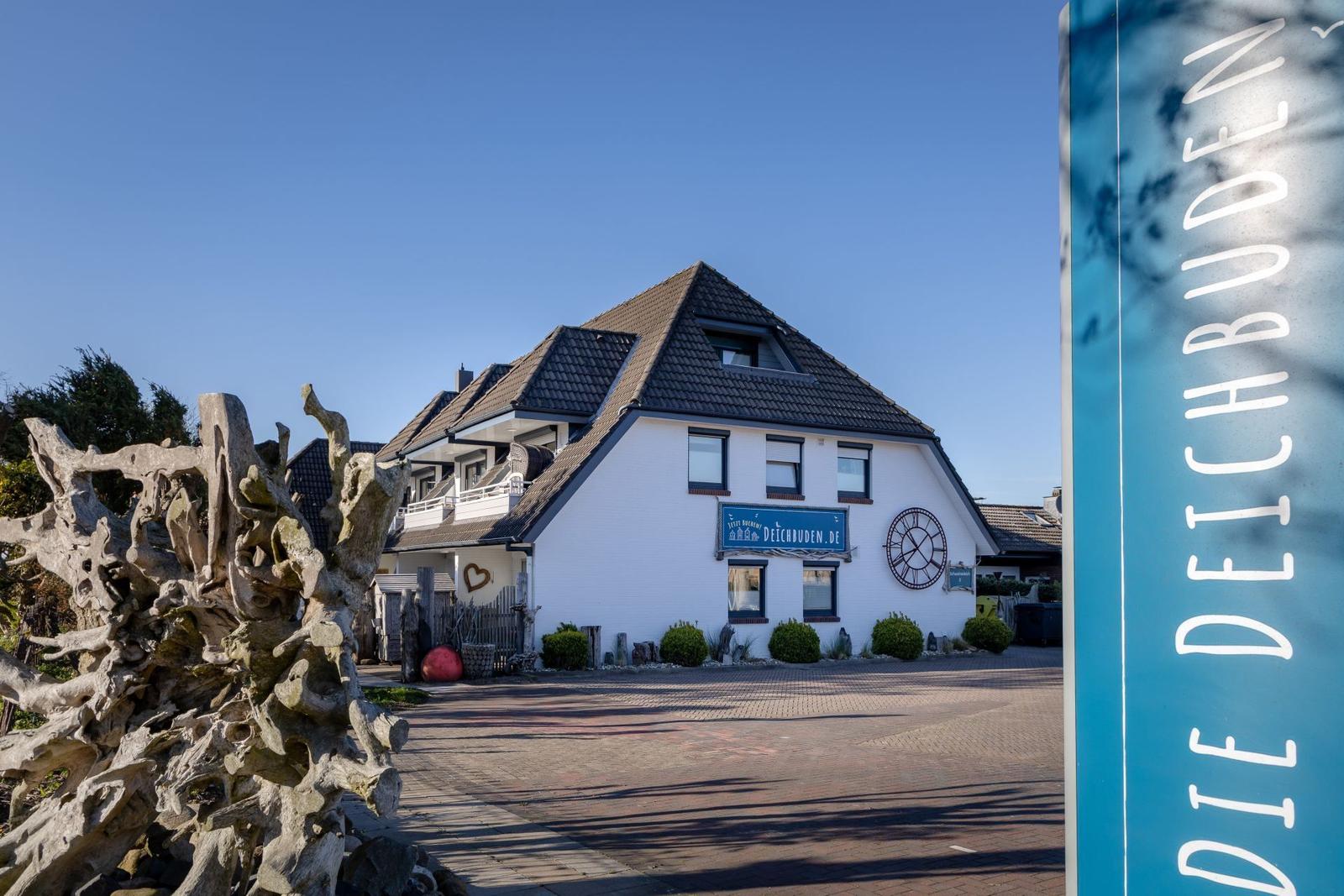 Weißes Haus mit Dach und Schild. Vorhof mit Holzskulptur und Straßenschild.