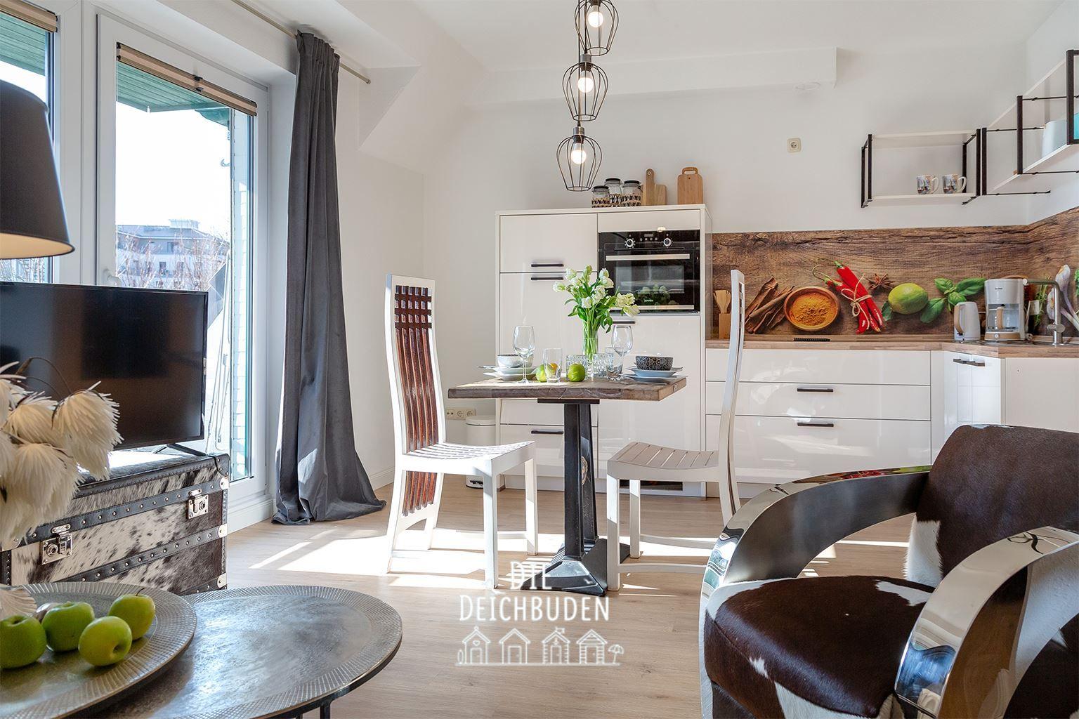 Küche mit Essbereich, TV und Sitzgelegenheiten. Holz- und Metallmöbel, Fenster mit Blick.