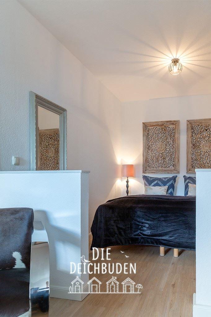 Schlafzimmer mit Bett, Wandbildern und Spiegel. Holzboden und Deckenleuchte.