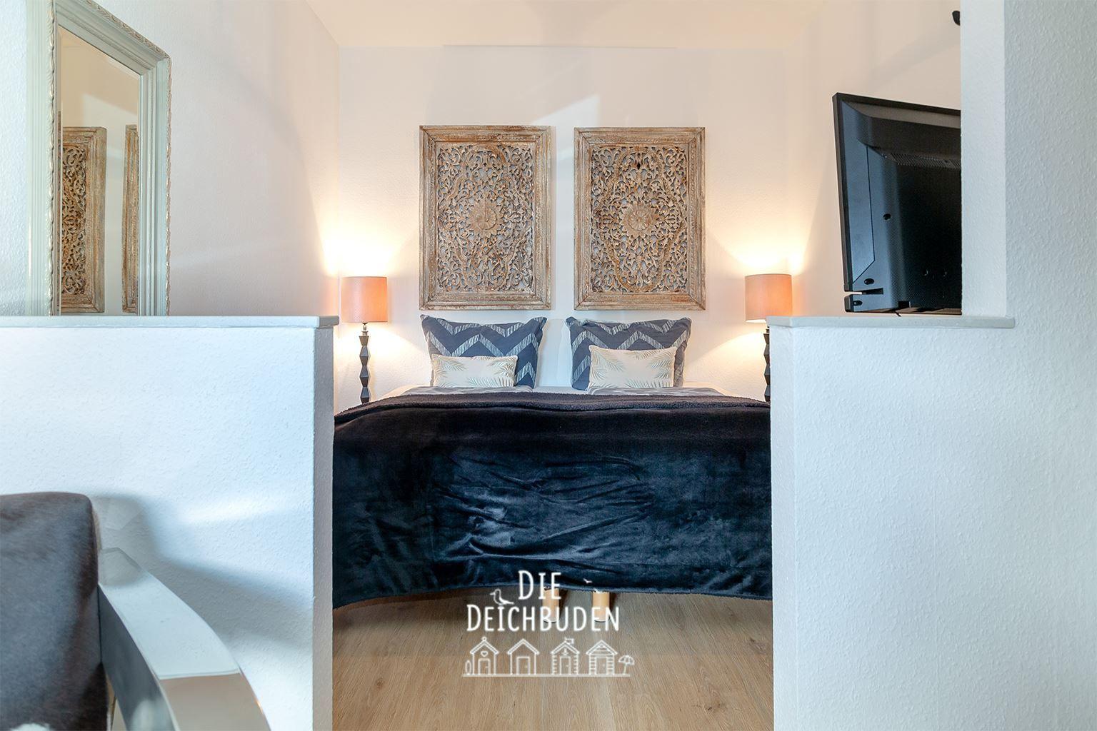 Schlafzimmer mit Bett, zwei Wandkunstwerken und Fernseher an der Wand.