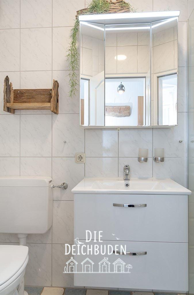 Badezimmer mit Waschbecken, Spiegelschrank und Toilette. Holzregal und Pflanze an der Wand.