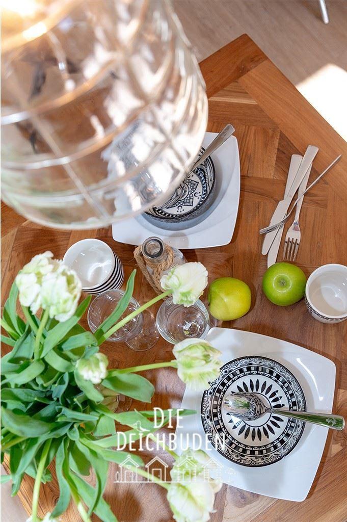 Holztisch mit Platzset, Tulpen, Äpfeln und Glasbehälter.