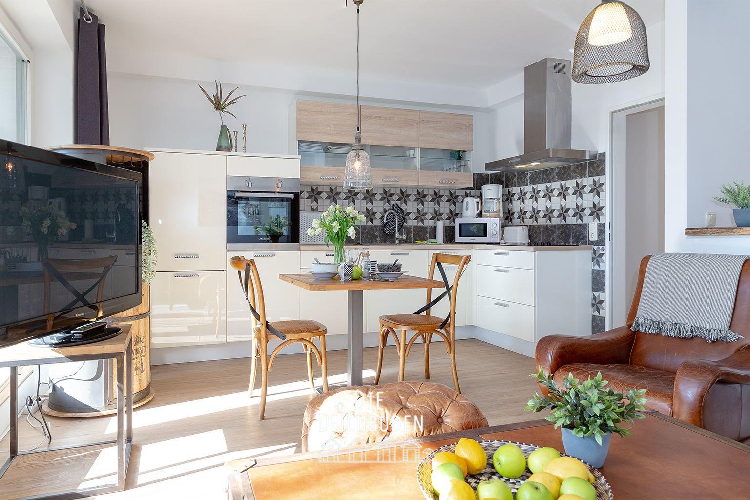 Küche mit Essbereich und Wohnbereich. Holztisch, Stühle, Sofa, Fernseher und Küchengeräte.