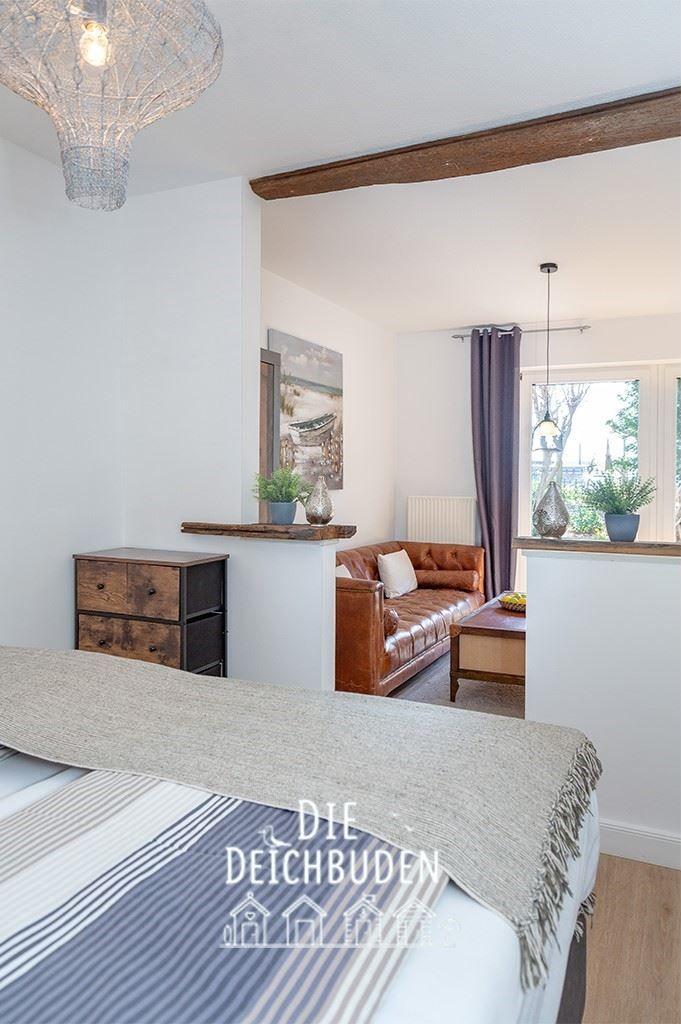 Schlafzimmer mit Bett und Blick auf Wohnbereich mit Ledersofa und Fenster