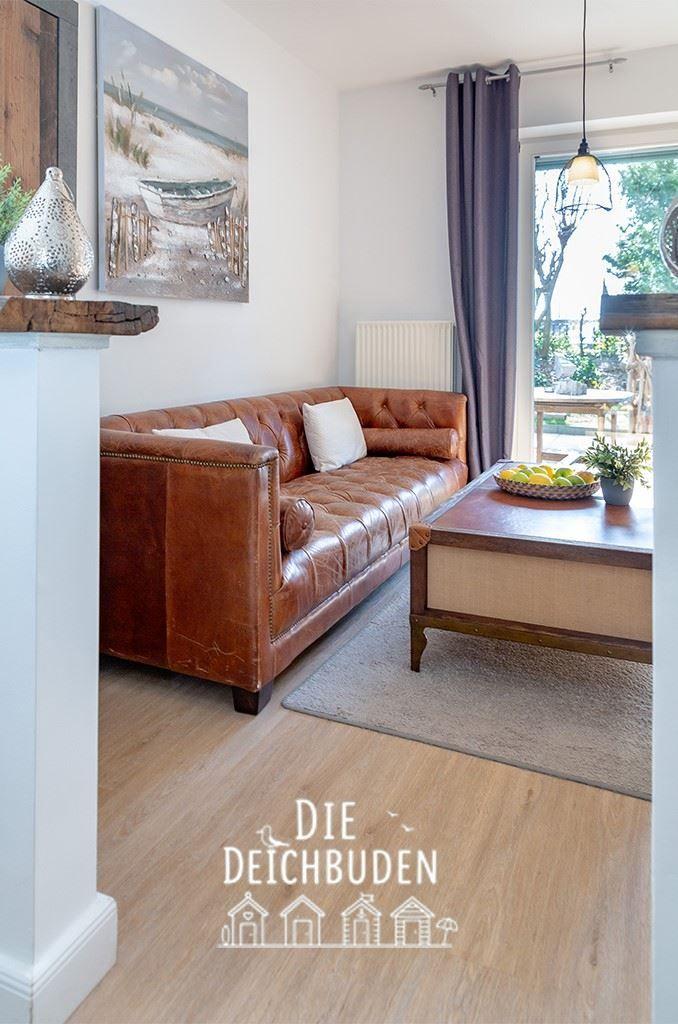 Lounge mit braunem Ledersofa, Holztisch und Wandbild. Durchgang zu Terrasse.