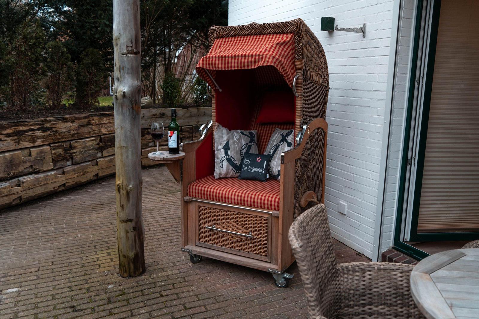 Hochwertiger Rattan-Sessel mit rotem Stoffbezug und Getränkehalter auf Terrasse.