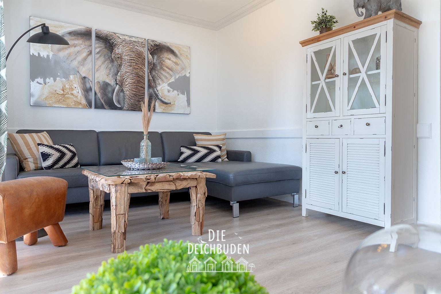Ein Wohnzimmer mit grauem Sofa, rustikalem Tisch und weißen Schränken.