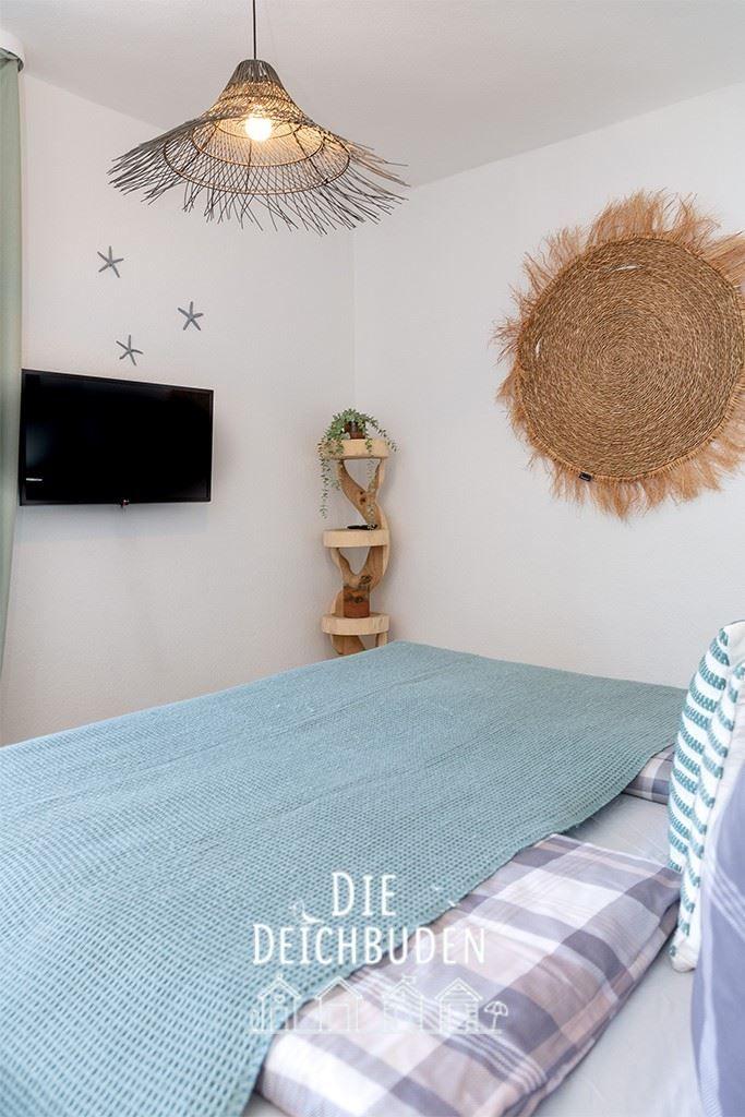 Schlafzimmer mit Bett, Wandfernseher, Pflanzenregal und Deckenleuchte.