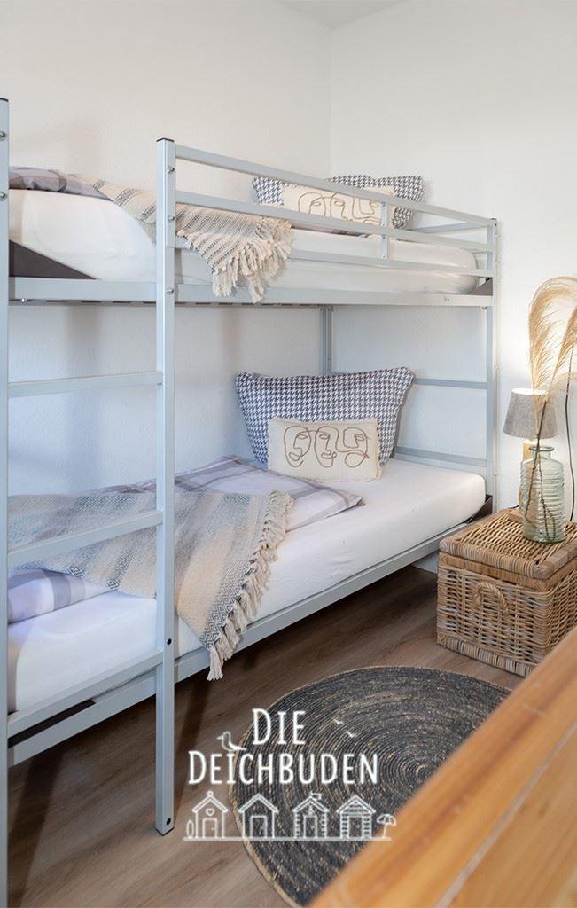 Doppelstockbett mit Matratzen, Kissen und Decken. Holzfußboden und Korb neben dem Bett.