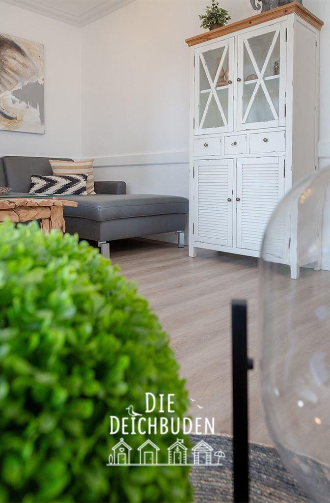 Ein Wohnzimmer mit grauem Sofa, Holztisch und weißem Schrank mit Glasfront.