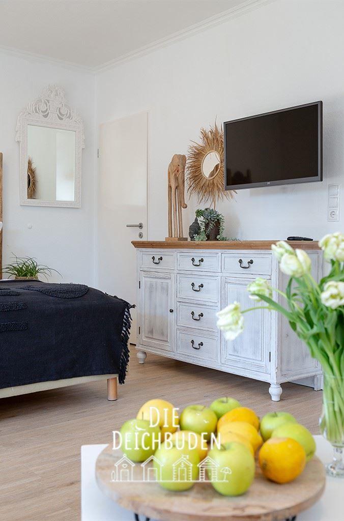Schlafzimmer mit Bett, Schrank und Fernseher. Auf dem Tisch stehen Äpfel und Zitrusfrüchte.