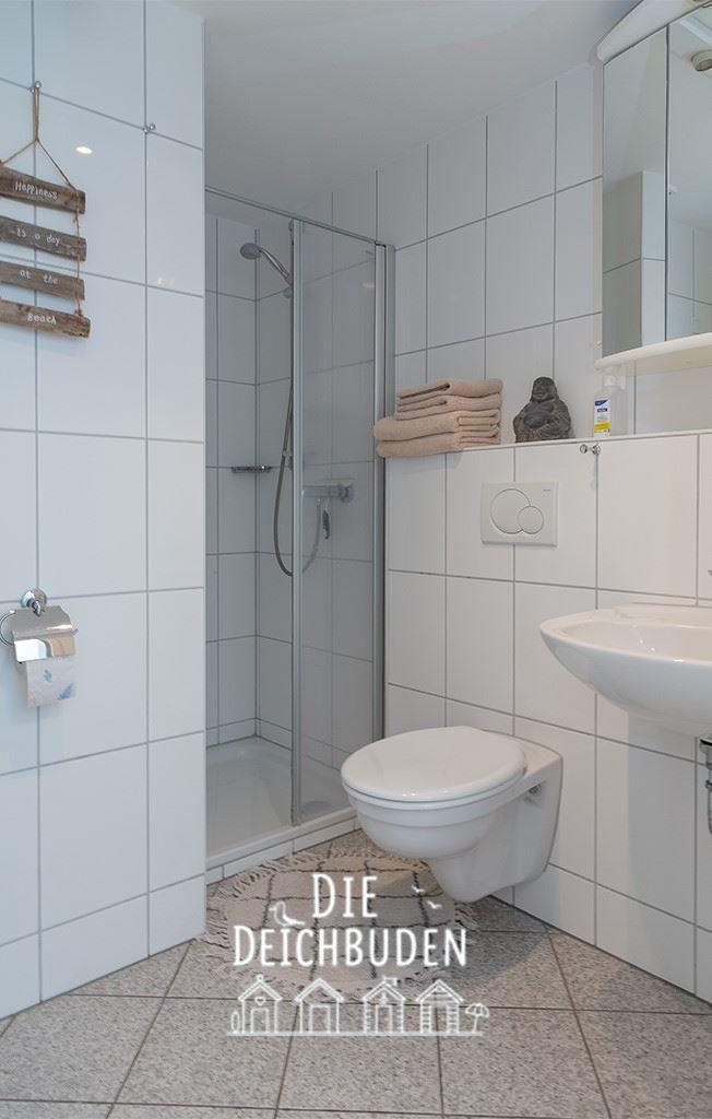 Badezimmer mit Dusche, Toilette und Waschbecken. Weiße Fliesen und Handtuch.